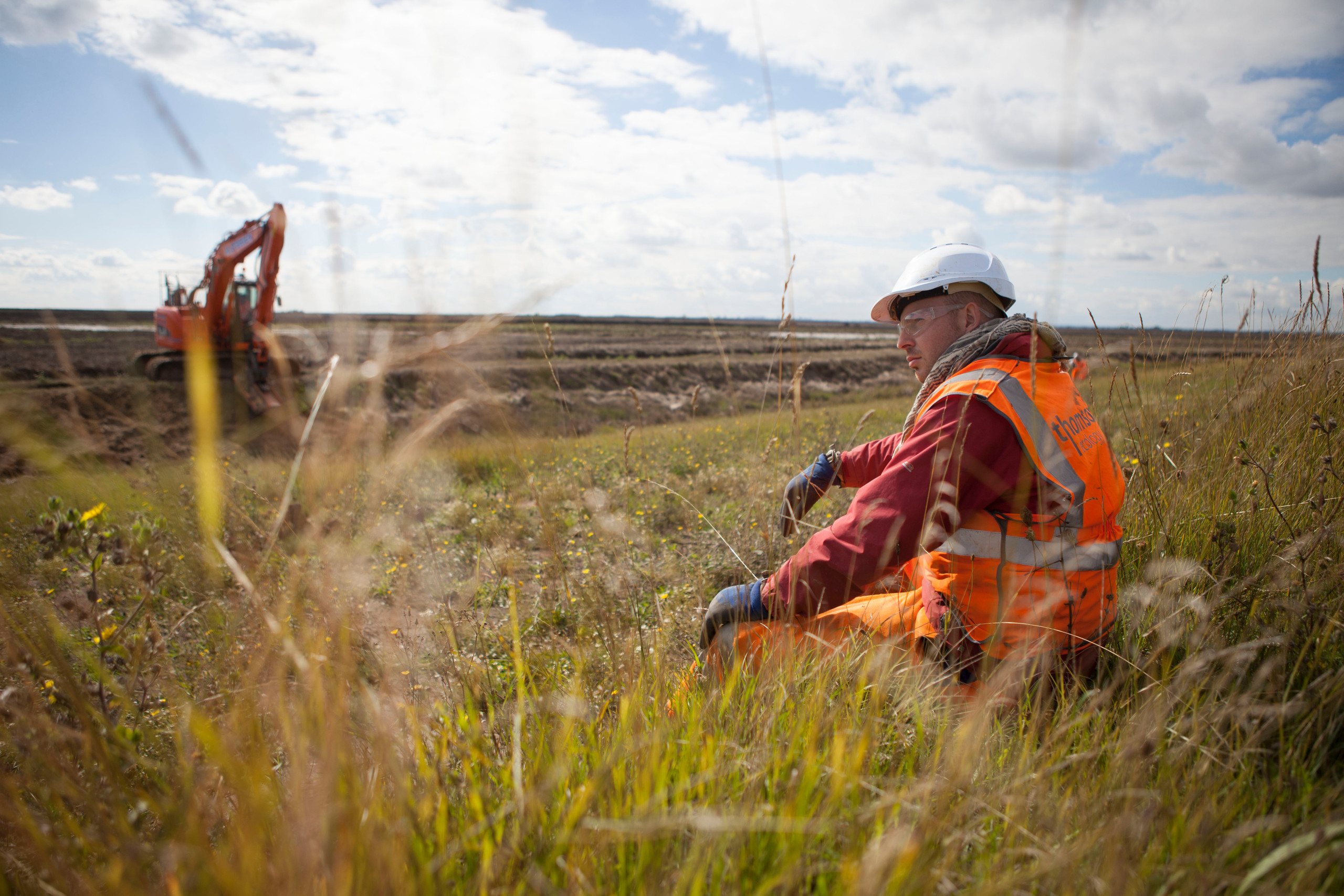 Photo of worker sitting in grass at Wallasea Island with an excavator in the background
